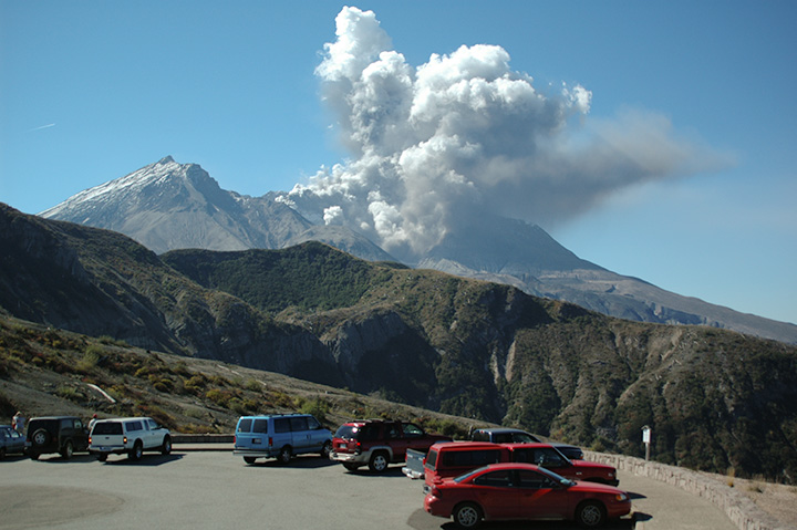 Mt. St. Helens Eruption, Oct. 1, 2024 volcano venting steam and ash under clear daytime sky and cars in the parking lot